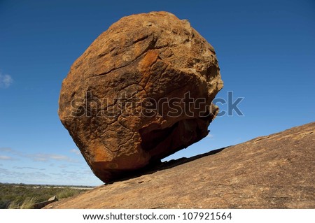 Against all odds, gravity or not, big boulder balancing on steep rocky hill, isolated with blue sky as background and copy space.