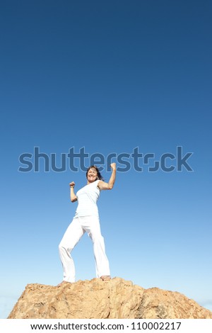 Strong and confident attractive mature woman on top of a mountain, isolated with blue sky as background and copy space.