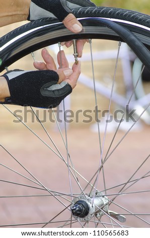 Close up image of a bicycle repair, with two hands in biker gloves, with valve, tube, alloys and a bike in the blurred background.