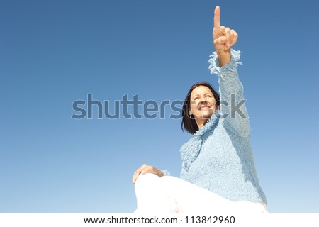 Happy confident and focused mature woman pointing with finger, isolated with blue sky as background and copy space.