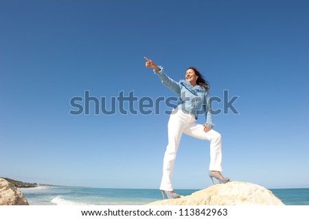 Positive confident happy mature woman in sexy high heel shoes on rock, isolated with ocean and blue sky as background and copy space.