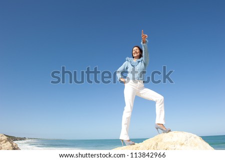 Positive confident happy mature woman in sexy high heel shoes on rock, isolated with ocean and blue sky as background and copy space.