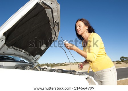 Stressed mature woman breakdown with car on remote road checking oil and waiting for assistance, for help, isolated with blue sky as background and copy space.