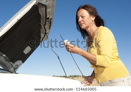 Stressed mature woman breakdown with car on remote road checking oil and waiting for assistance, for help, isolated with blue sky as background and copy space.