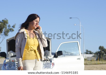 Stressed mature woman breakdown with car on remote road calling for service, assistance, for help on mobile phone, isolated with blue sky as background and copy space.
