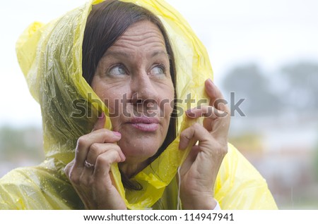 Portrait mature woman standing in the rain, wearing yellow raincoat, isolated with grey sky as background and copy space.
