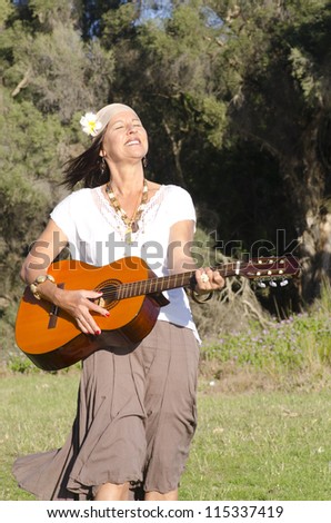 Portrait of beautiful mature hippie woman with guitar outdoor in park, enjoying leisure lifestyle, isolated with green blush vegetation as background and copy space.