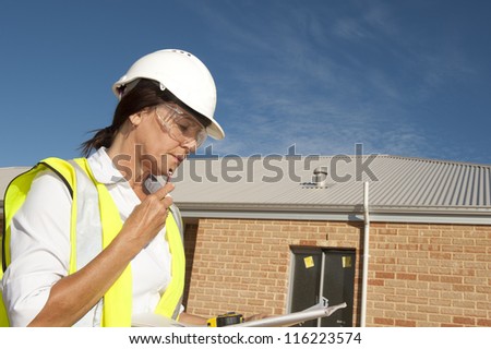 Female architect on construction site, supervising building of residential houses, isolated with brick wall and blue sky as background and copy space.