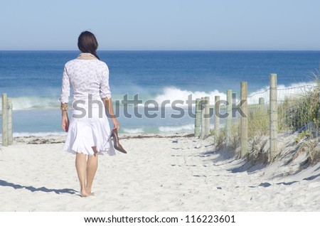 Attractive senior woman happy and joyful at beach, relaxed with high heel shoes in hand, isolated with ocean and blue sky as background and copy space.
