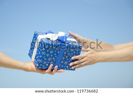 Outdoor Isolated christmas or birthday present with giving and receiving hands, with blue sky as background and copy space.