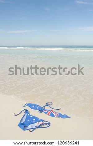 Sexy bikini with Australian flag design lying in the sand of a lonely and remote tropical beach, isolated with ocean and blue sky as background and copy space.