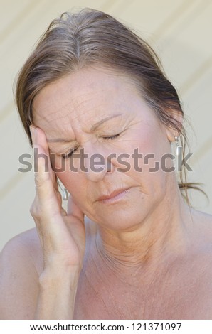 Outdoor portrait of concerned woman in pain, depression, in menopause with hand holding head, isolated with blurred background.