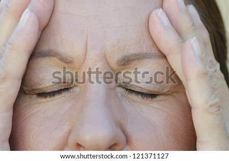 Close Up portrait of worried woman with closed eyes and hands on forehead.