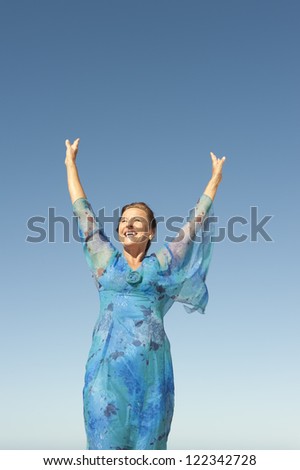 Portrait elegant middle aged woman sunny day outdoor, happy smiling with joyful arms up and isolated with blue sky as background and copy space.