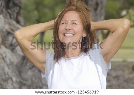 Portrait fit and healthy, confident and happy attractive middle aged woman with arms up, with blurred background outdoor.