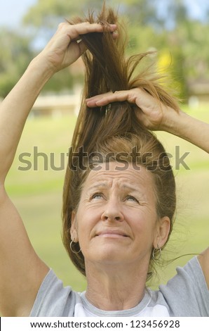 Attractive middle aged woman tearing her hair, with worried and concerned facial expression and blurred background outdoor.