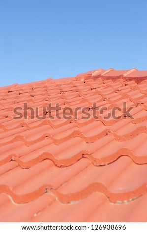 Roof with red tiles and shingles, upward view along gable, with clear blue sky as background and copy space.