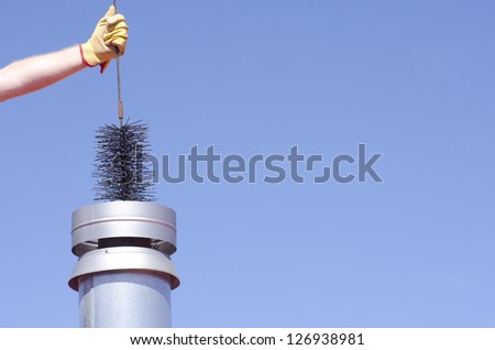 Arm with yellow glove holding sweeper to clean chimney on house, isolated with blue sky as background and copy space.
