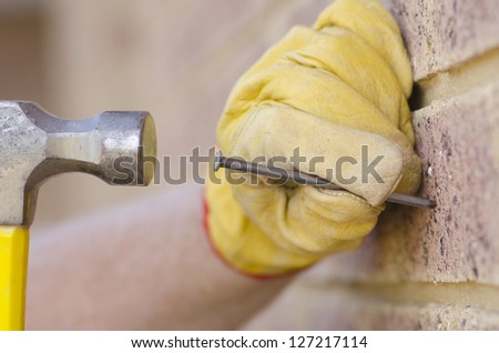 Closeup of hand in gloves with nail and hammer and brick wall as blurred background plus copy space.