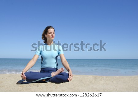 Beautiful sexy young girl sitting in cross-legged yoga lotus pose at a remote tropical beach. Clear blue sky with copy space