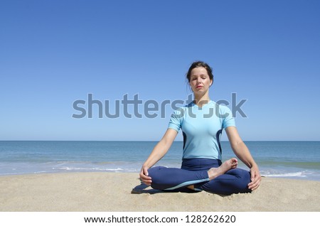 Beautiful sexy young girl sitting in cross-legged yoga lotus pose at a remote tropical beach. Clear blue sky with copy space