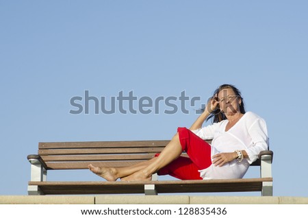 Portrait relaxed and beautiful looking mature woman resting at sunny day on bench outdoor, with clear blue sky as background and copy space.