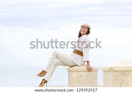 Portrait attractive happy friendly mature woman in high heel shoes enjoying relaxed active retirement at beach, isolated with ocean and white cloudy sky as background and copy space.