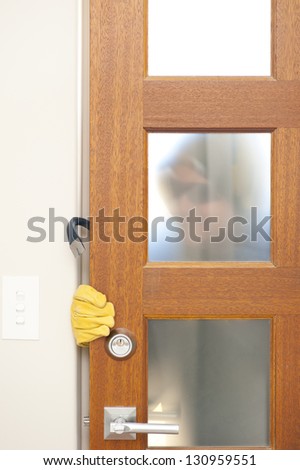 Burglar, thief  with gloves, holding crowbar breaking into home, unlock door, blurred visible silhouette behind milky windows, with copy space.