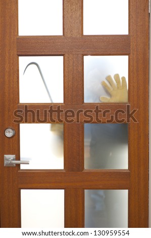 Hands of Burglar, thief  with gloves, holding crowbar trying to break in home, unlock door, blurred visible silhouette behind milky windows, with copy space.