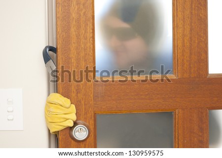 Burglar, thief  with gloves, holding crowbar breaking into home, unlock door, blurred visible silhouette behind milky windows, with copy space.