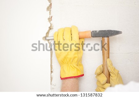 Workers hands with yellow gloves repairing, renovating interior wall in house with hammer and bite or chisel or gouge.
