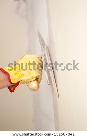 Closeup of palette-knife or scraper and cement filling for house renovation construction in hands of handyman and worker fixing interior wall, with blurred background and copy space.