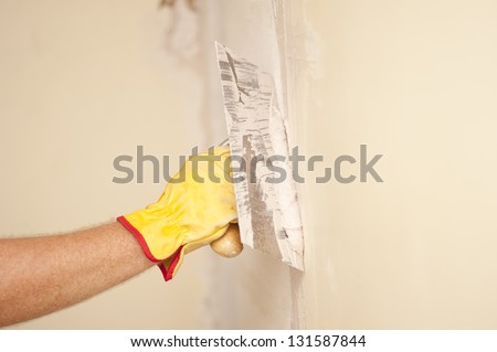 Closeup of palette-knife or scraper and cement filling for house renovation construction in hands of handyman and worker fixing interior wall, with blurred background and copy space.