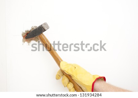 Hammer in hand with gloves of man smashing hole in white home brick wall, demolishing, damaging house room, isolated with white background and copy space.