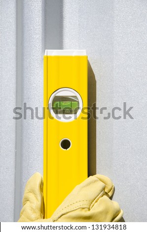Hand of construction worker with glove on spirit or water level tool outdoor, with silver metal wall as background and copy space.
