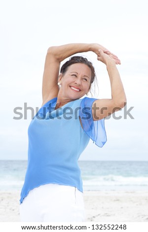 Portrait Beautiful mature woman confident and happy at beach, wearing blue blouse, with ocean and white overcast sky as blurred background and copy space.