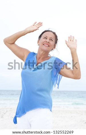 Portrait Beautiful mature woman joyful and happy at beach, wearing blue blouse, with ocean and white overcast sky as blurred background and copy space.