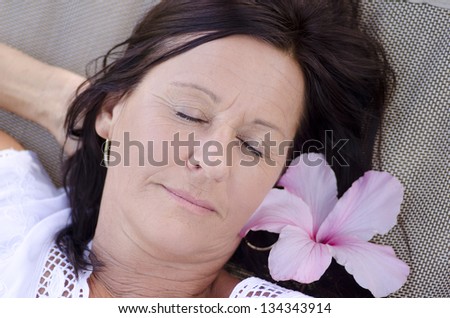 Portrait beautiful mature woman sleeping, with smiling happy and relaxed facial expression, closed eyes and flower in hair.