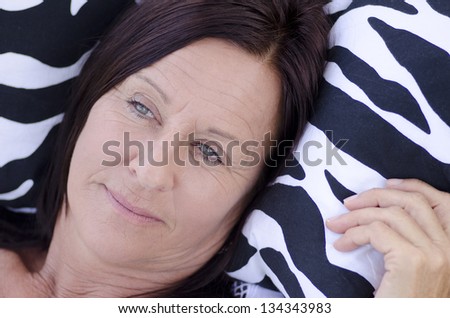 Portrait beautiful mature woman  with sad and lonely facial expression, lying alone and thoughtful on cushion.