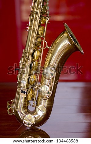 Shiny golden shimmering saxophone on polished wooden floor, isolated with red background and optical reflection.