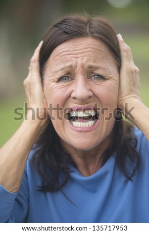 Portrait attractive mature woman covering frustrated, angry or in anxiety her ears with hands, upset stressed, isolated with blurred outdoor background.
