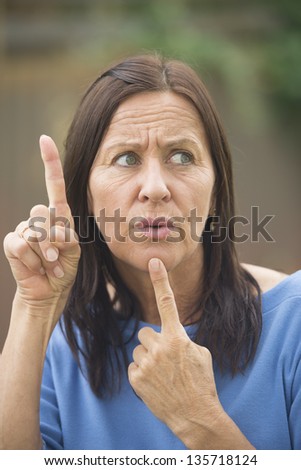 Portrait beautiful mature woman outdoor with worried facial expression, thoughtful, finger up and at chin, isolated with blurred background.
