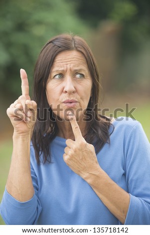 Portrait attractive mature woman outdoor with worried facial expression, thoughtful, finger up and at chin, isolated with blurred background.