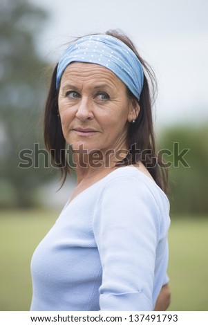 Portrait beautiful looking senior woman with headband posing outdoor in park, friendly, happy and relaxed smiling, with copy space and blurred background.