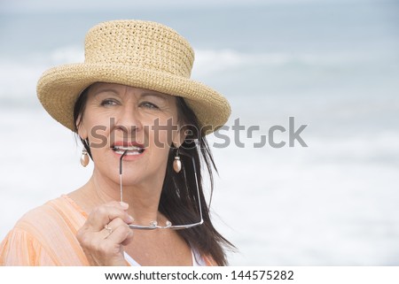 Portrait attractive mature woman with summer hat, orange blouse, thoughtful daydreaming, relaxed and confident, with blurred background outdoor.