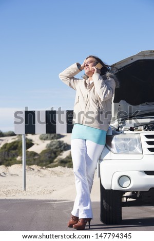 Portrait stressed mature woman breakdown with car calling for service, assistance for help on mobile phone, with blue sky as background and copy space.