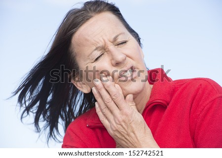Portrait attractive middle aged woman outdoor in stress and pain, dental problems, suffering from toothache, pressing hands on chin.