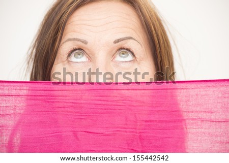 Portrait attractive middle aged woman hiding behind pink cloth, with upward view and beautiful eyes, white background.
