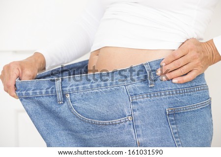 Torso of woman showing proud result of weightloss through successful dieting, wearing over sized jeans and shirt, isolated on white.