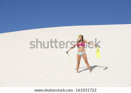 Portrait active attractive middle aged woman with snorkel gear and bikini lost and worried on desert sand dune, with blue sky as background and copy space.